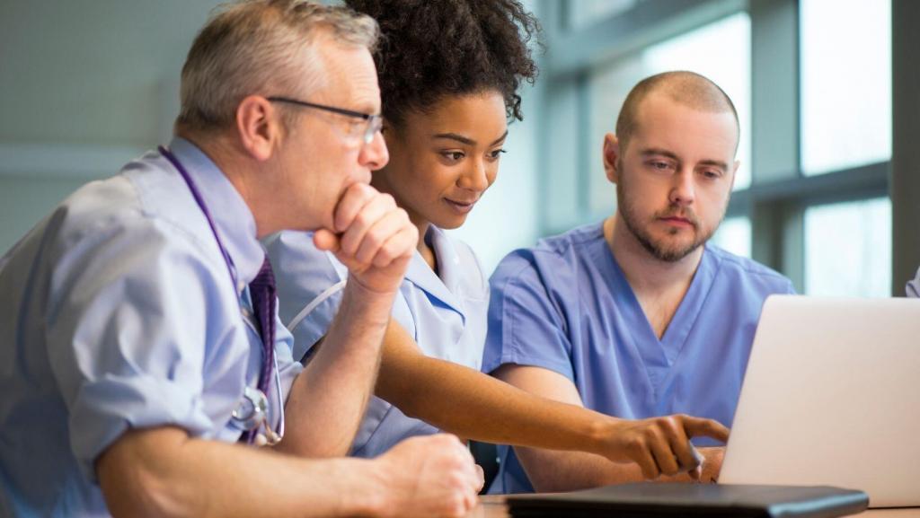 aesthetic professionals in scrubs around a laptop