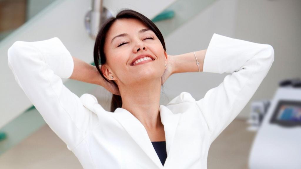Woman wearing white blazer smiling with her hands behind her head with body contouring machine in the background