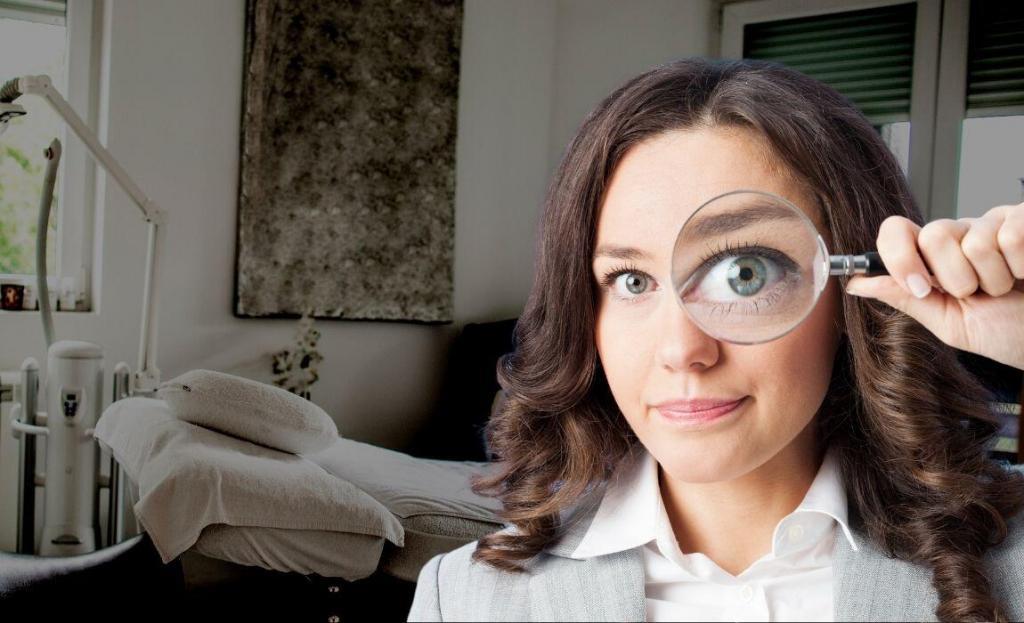 woman holding magnifying glass with an aesthetic treatment room in the background