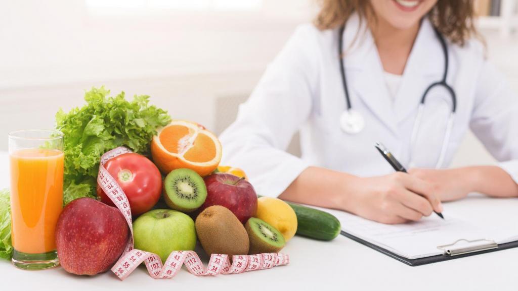 Body contouring professional wearing a lab coat and stethoscope writing diet recommendations with fruit and measuring tape beside her