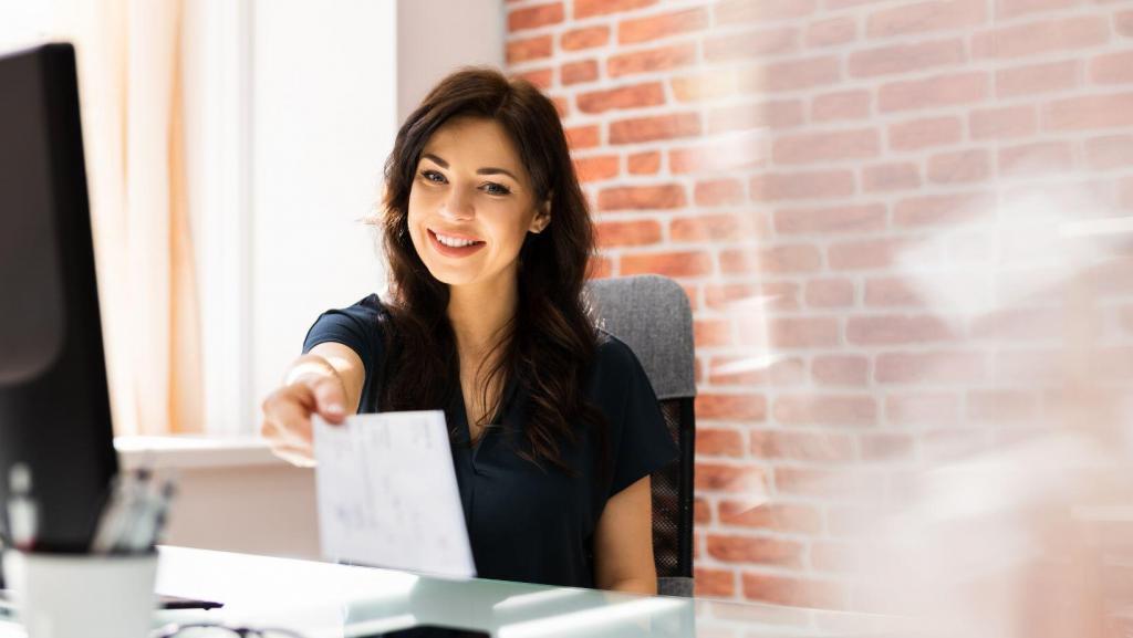 Happy woman sitting behind desk handing out a pay check