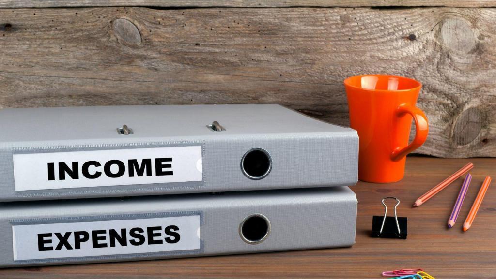 notebooks titled "income" and "expenses" laying on a desk with an orange mug and pencils laying beside them