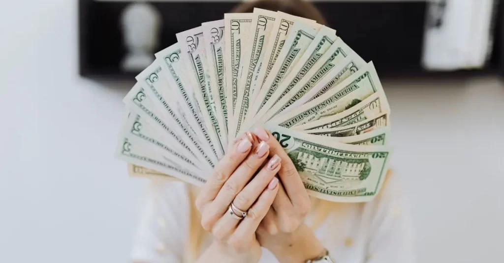 woman holding a fan of dollar bills in front of her face