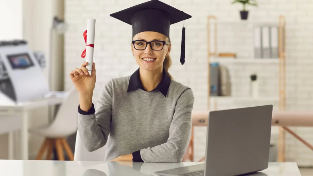 woman in graduation cap in front of laptop holding certification from the body contouring academy
